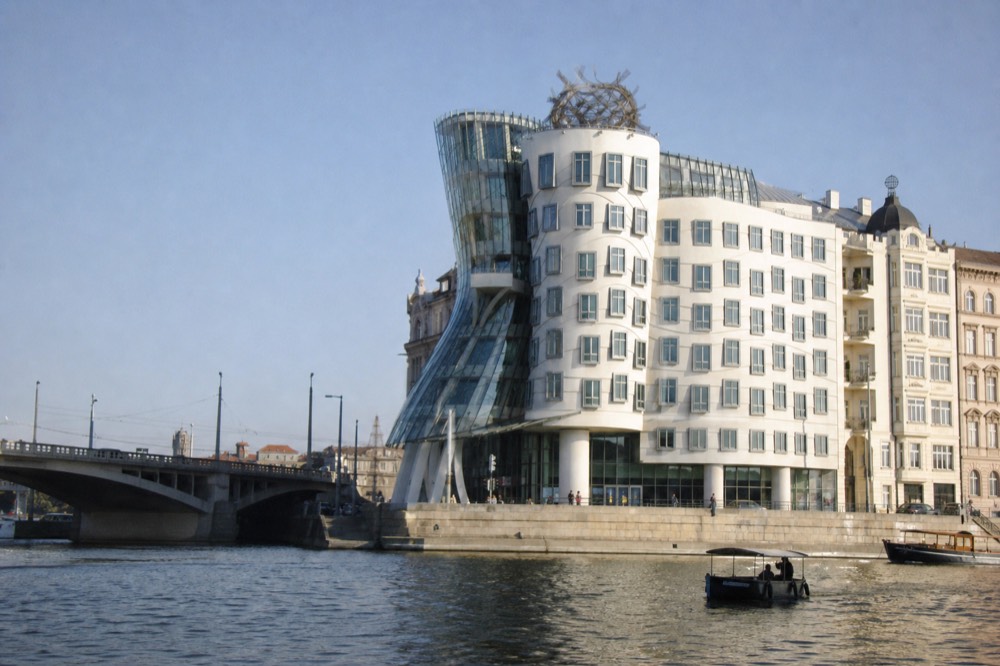 The Dancing House's curved glass form seen from the river at midday, hard sun on the glass