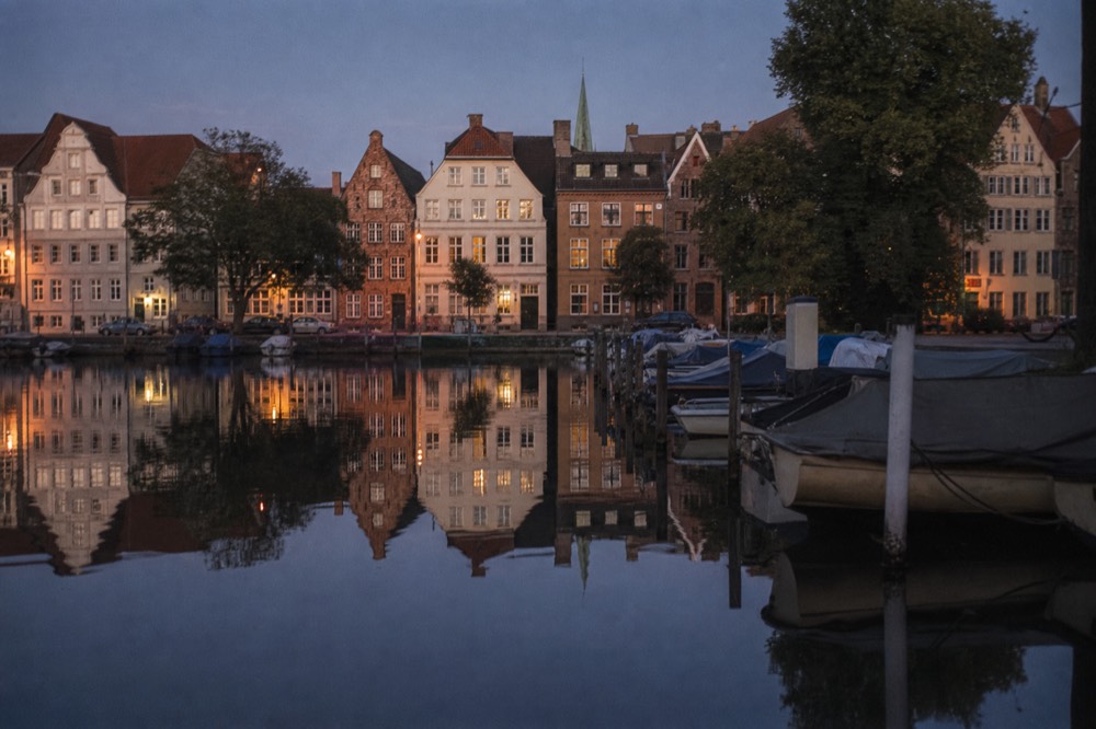Mirror-still water reflecting the Old Town facades at dusk, the reflected windows glowing amber, barely a ripple to break the symmetry