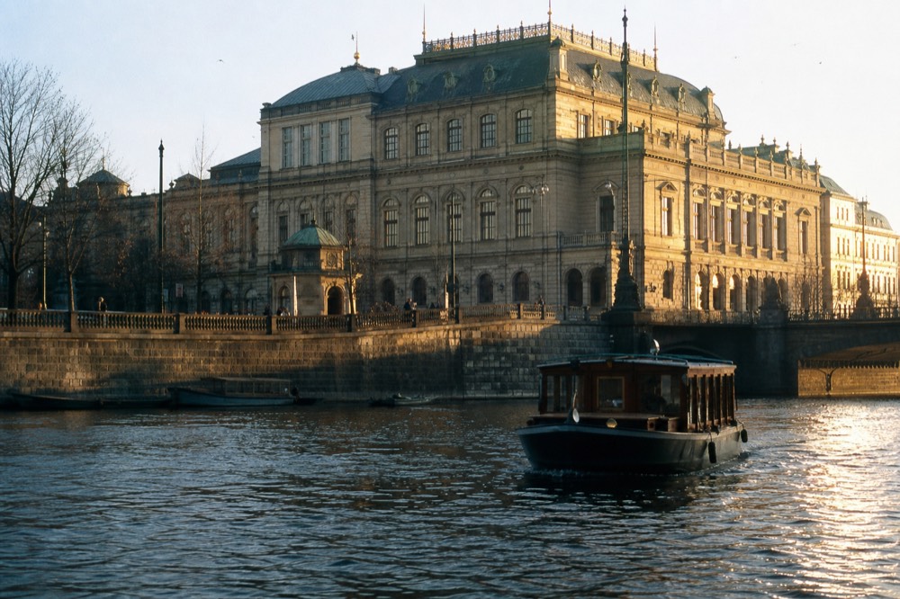 The Rudolfinum concert hall's stone facade seen from the water in soft morning light