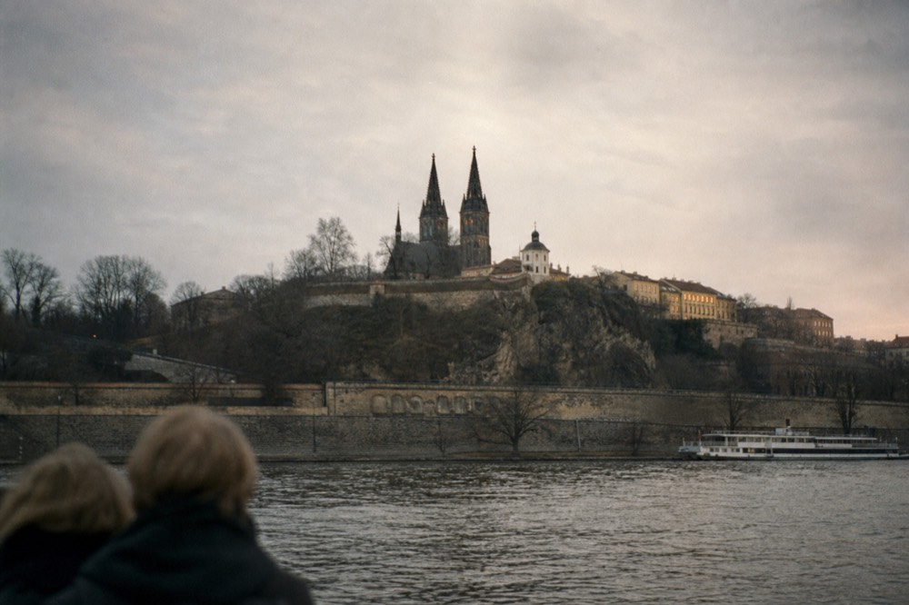 Vyšehrad's fortress walls on a bluff above the river, seen from a passing boat in hazy afternoon light